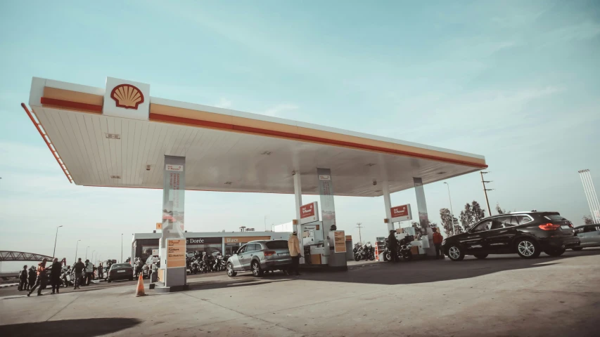 a car parked at a gas station, people on bikes, and motorcycles