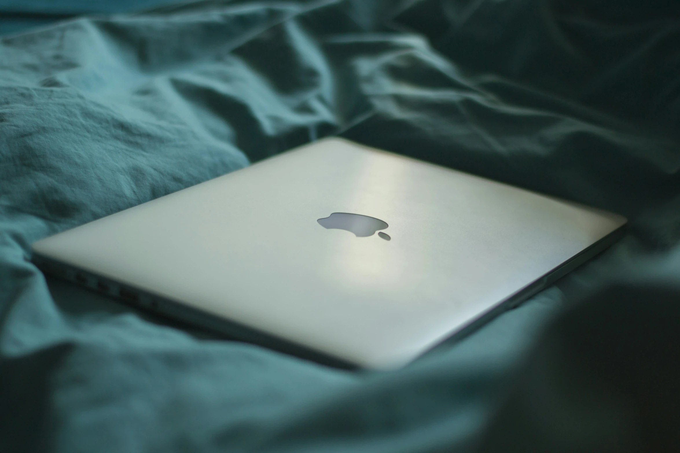 the back of an apple laptop computer laying on a bed