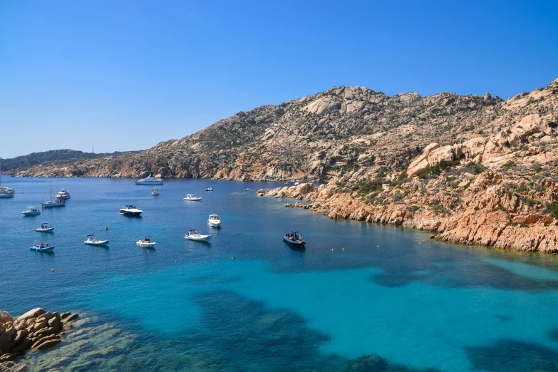 several small boats anchored at the shore next to a mountain