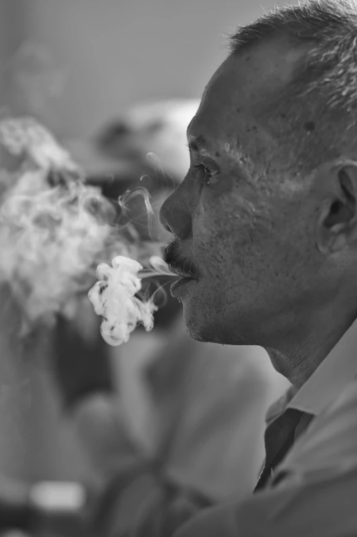 a man is blowing on a cigarette, while the man in the background looks at him