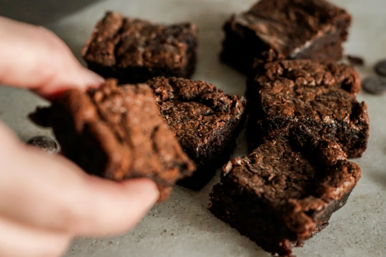 a person holding a piece of chocolate brownie on top of a plate