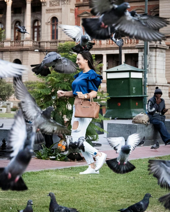 woman standing in front of pigeons on grass with buildings