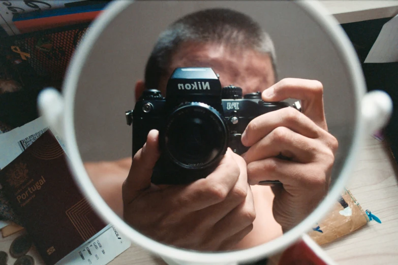 man holding camera reflected in round mirror near books