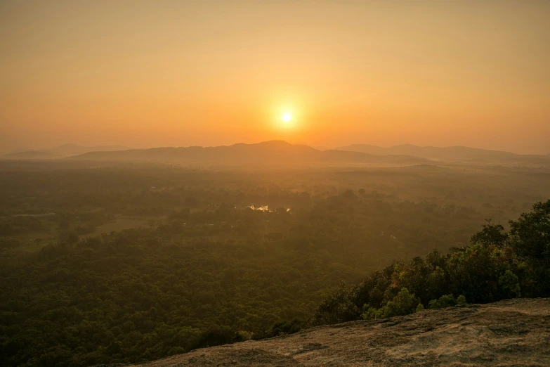 a sunset over trees and land, with a distant sky