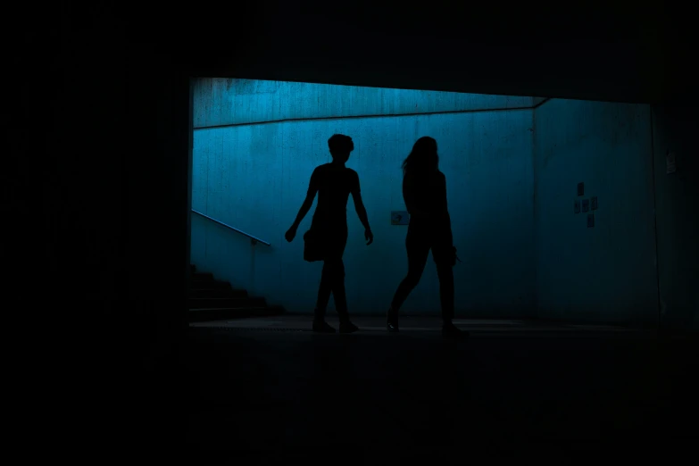 two dark haired people standing in a dark room