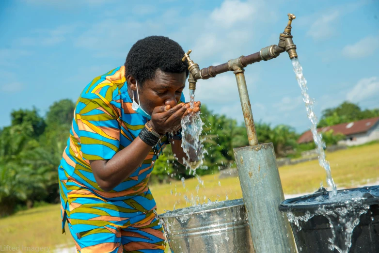 a woman in striped shirt drinking water from water fountain