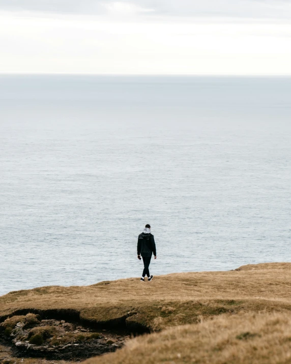 man in black jacket and backpack standing alone on top of an island