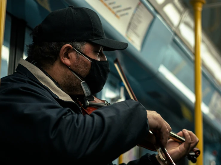 a man with a black hat and coat holding a cell phone while riding on a subway