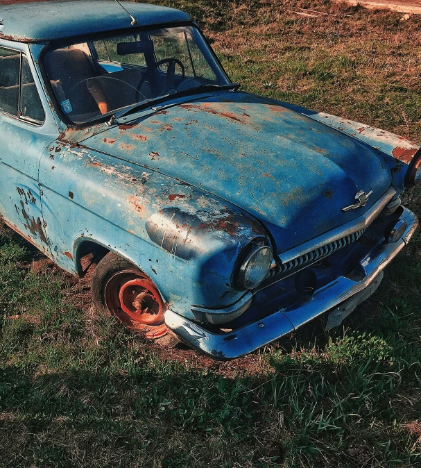 an old rusted, blue car sits on the ground