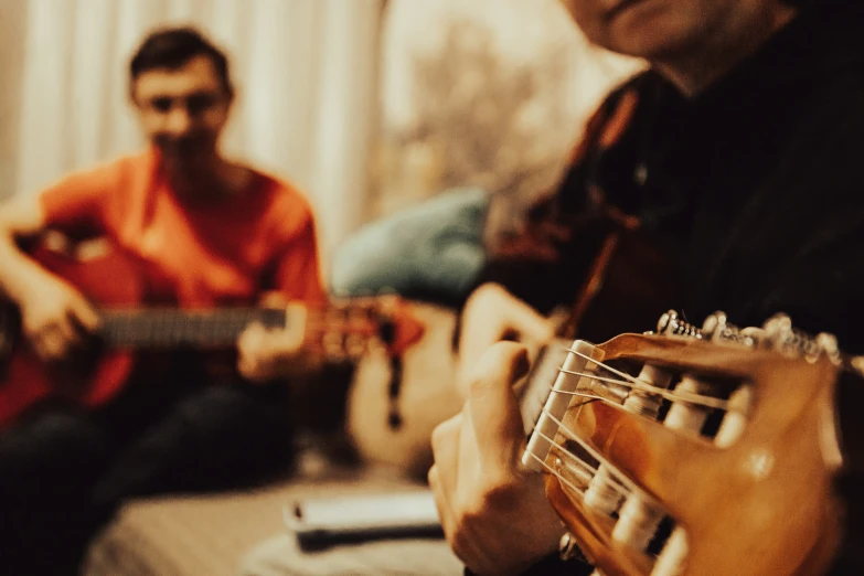 a man is playing an acoustic guitar while another man watches from the couch