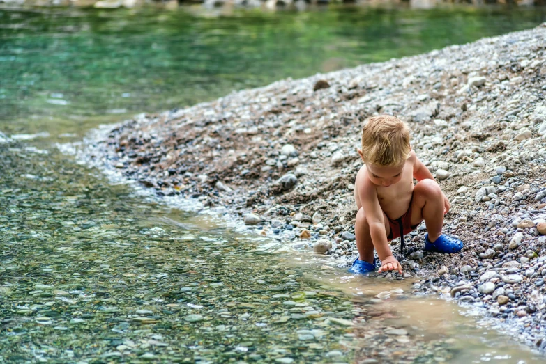 a young child crouched on a beach next to water