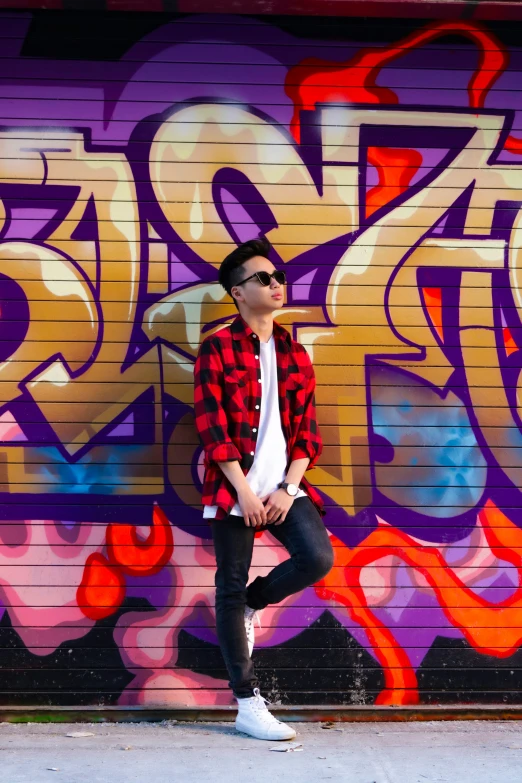 a man stands by a graffiti wall wearing a plaid jacket