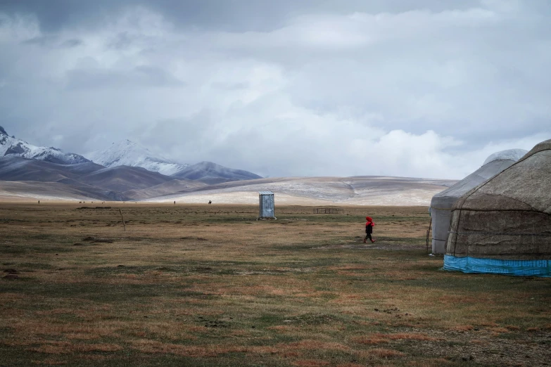 a tipie house next to an outhouse with some mountains in the background