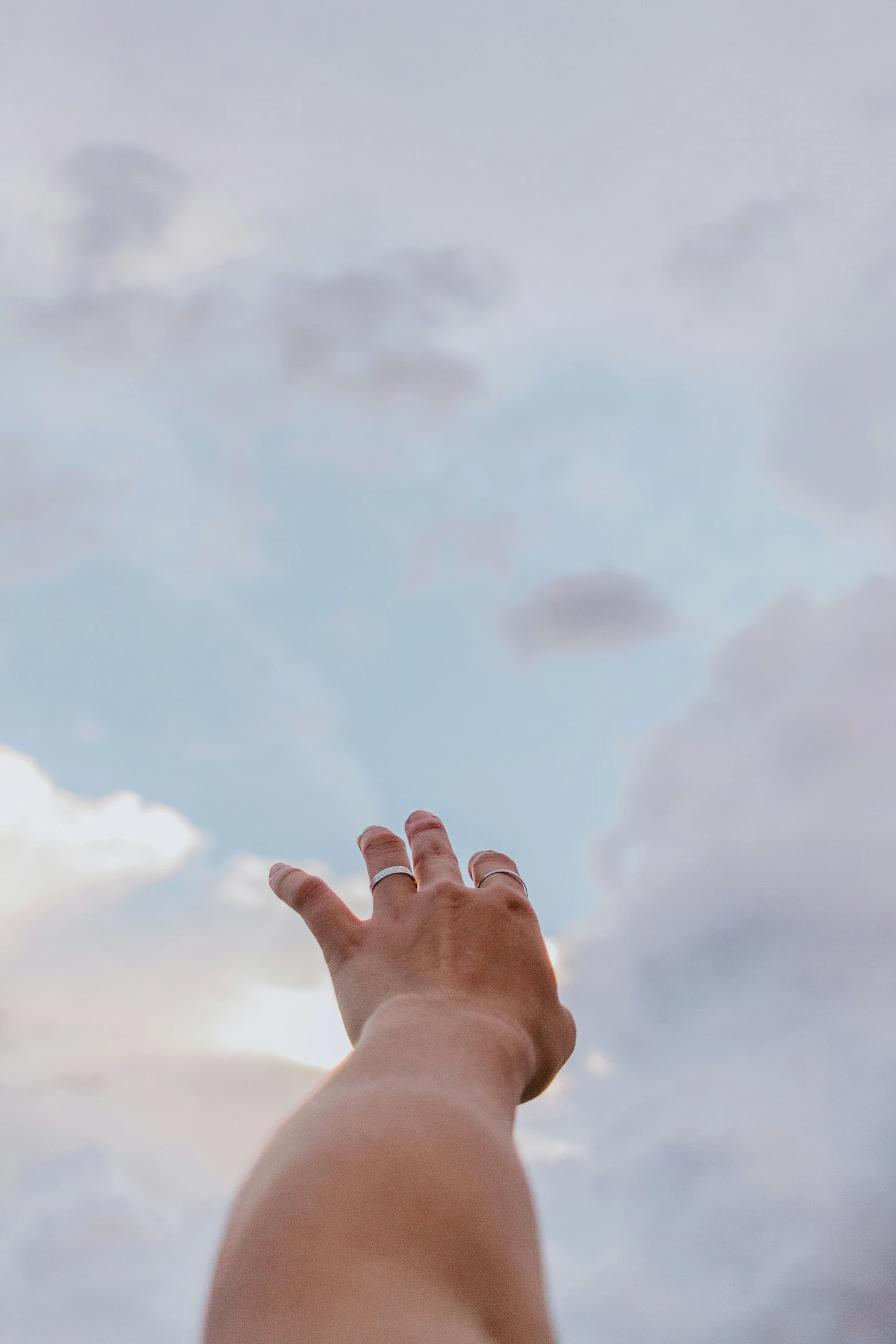 a hand reaching to the sky with clouds behind