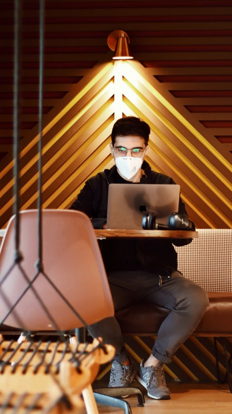 man with mask and laptop on chair in room