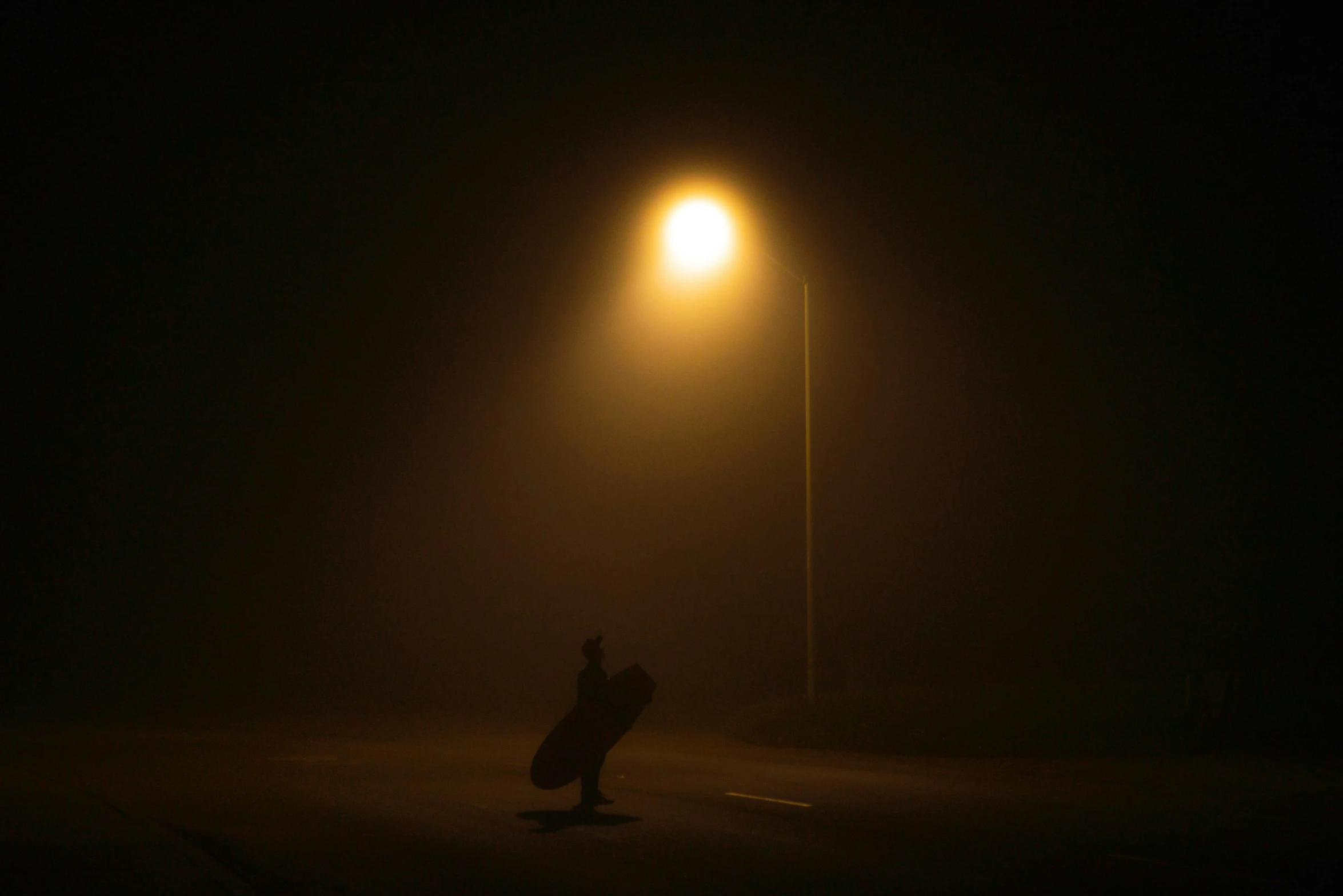 a dark city street at night with a person in the middle of the road standing under a street light