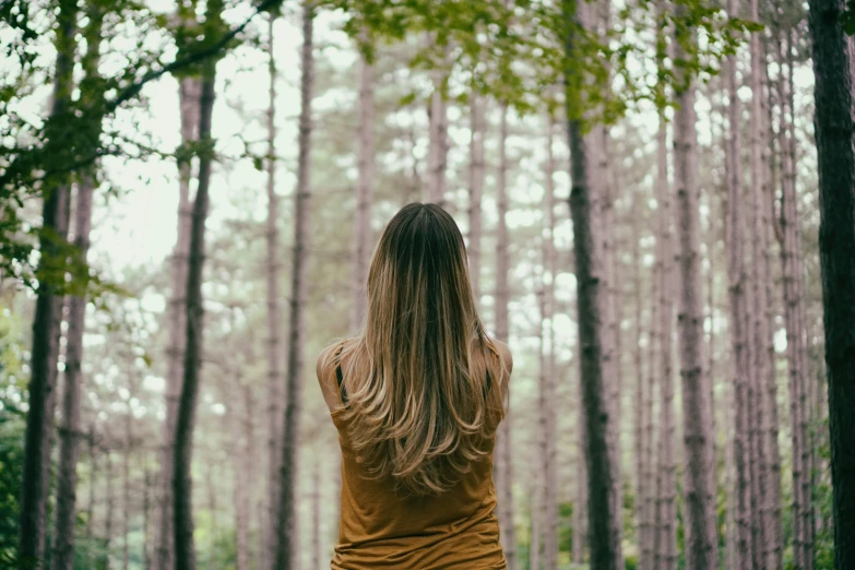 a woman looking at some trees in the woods