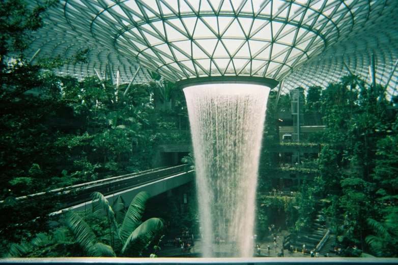 the waterfall is under a clear roof surrounded by greenery