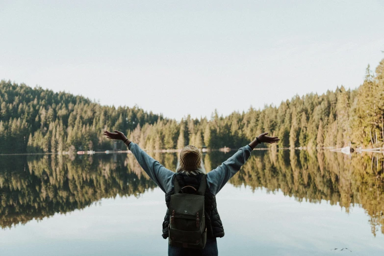 a person with their arms wide open standing in front of a lake