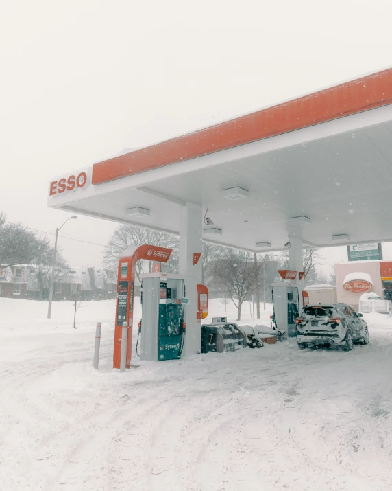 a snow covered gas station with two cars parked in the snowy parking lot