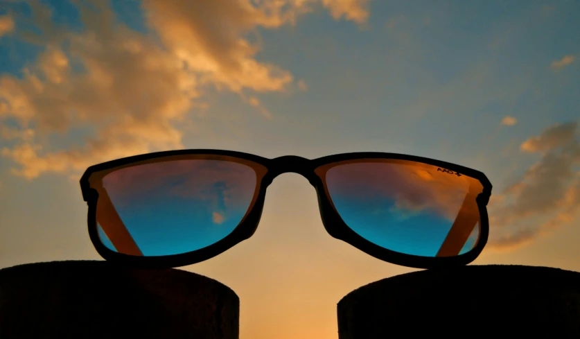 pair of sunglasses, each with reflection, over sunset sky