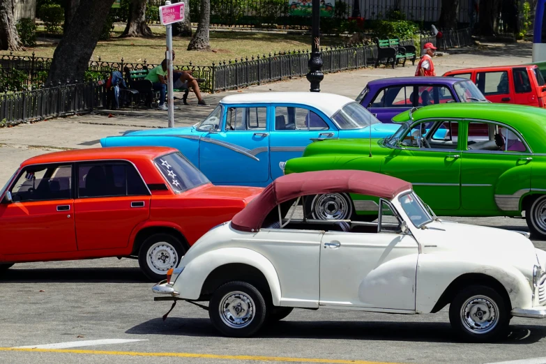 several colorful classic cars are lined up on the street