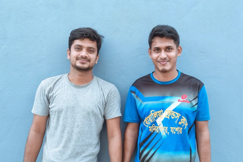 two young men standing next to each other in front of a blue wall