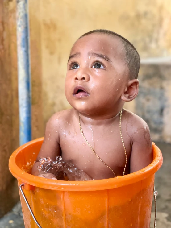 there is a little boy taking a bath in an orange tub