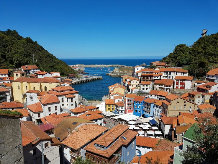 a town built on a hillside with some red roofs and the sea in the background