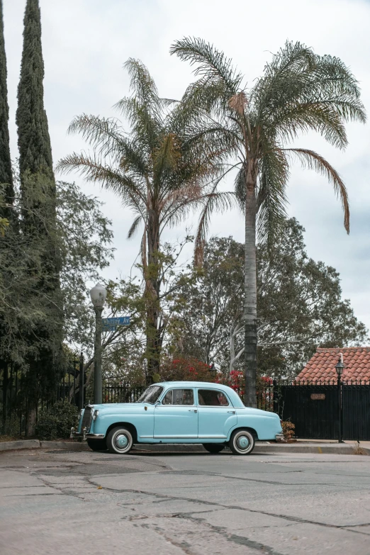 an old car parked by some palm trees in a street