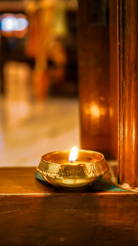 a golden lit candle sitting next to a brown pillar