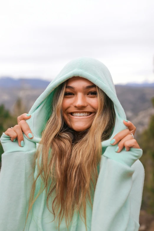 a woman with long hair smiles under the hoodie