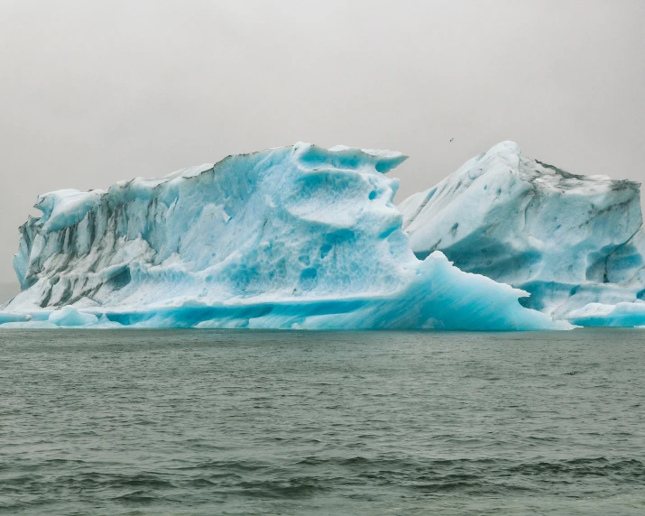 an iceberg in the water with a cloudy sky behind