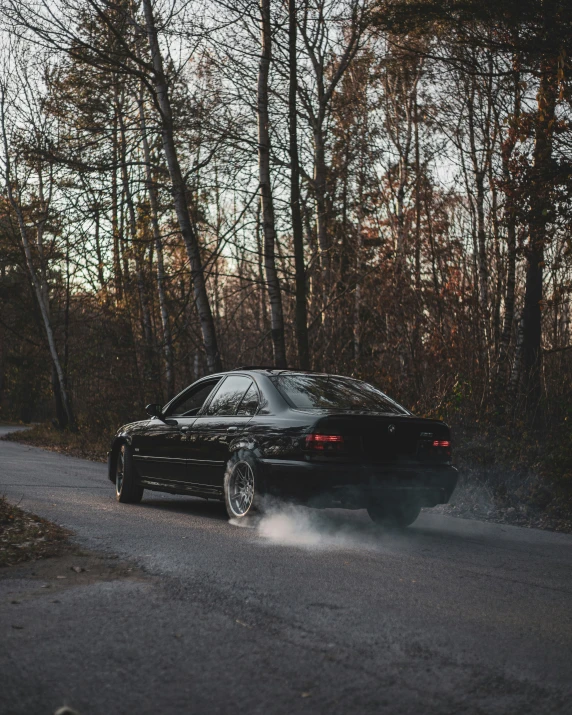 black car driving down a dirt road in front of tall trees