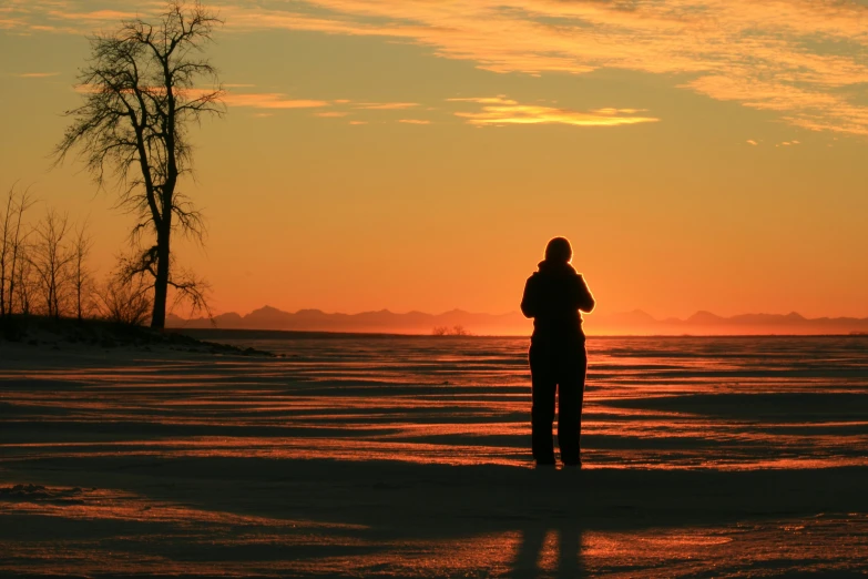 a person standing in front of a sunset on the frozen river