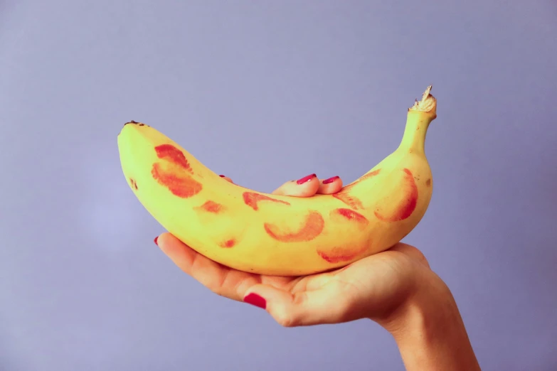 a hand is holding a yellow banana that has red dots