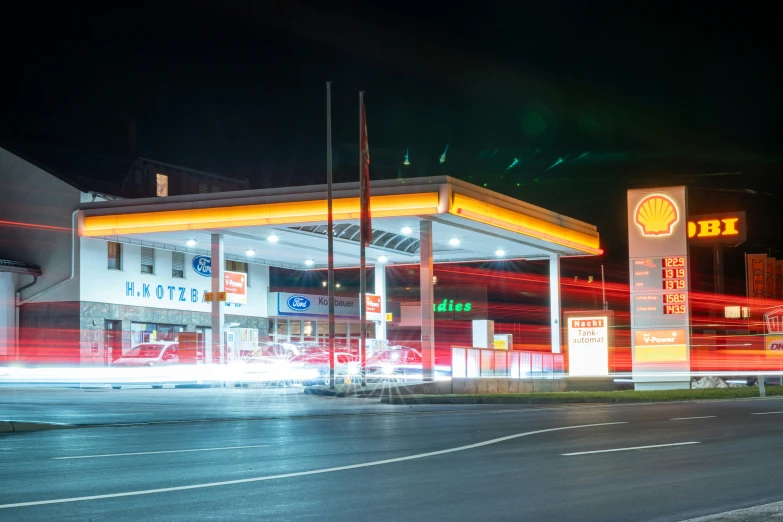 cars drive by the lit gas station