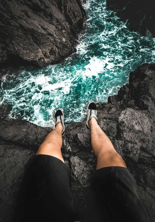 a person with their feet on the edge of rocks by water