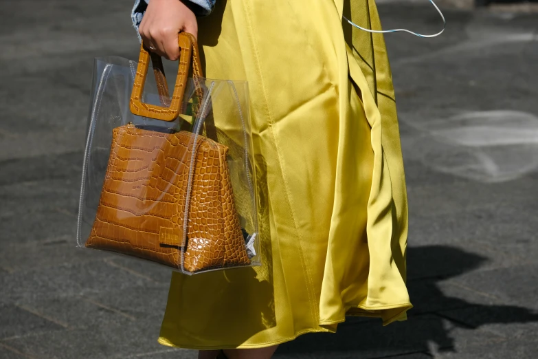 a woman with a yellow skirt and jacket is holding a brown purse