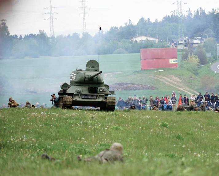 a group of people standing in a field watching two military tanks