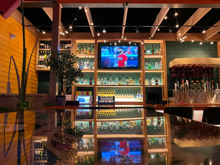 the inside of a bar with liquor glasses and television screen