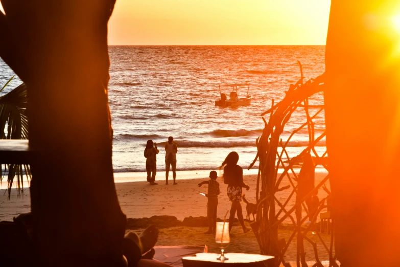 a beach scene with people standing on the sand and sitting at an outdoor dining table