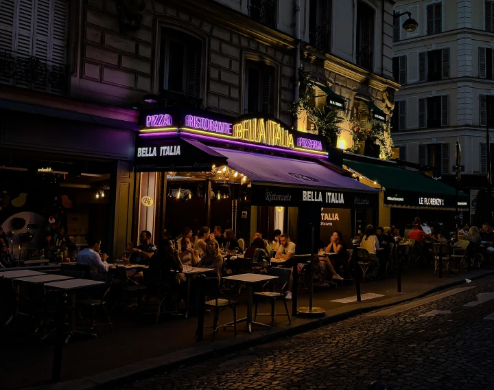 people sit at tables in an alleyway next to several buildings