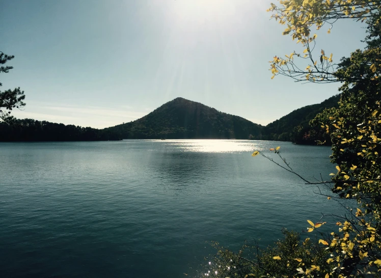 sun shining on water and mountain range behind