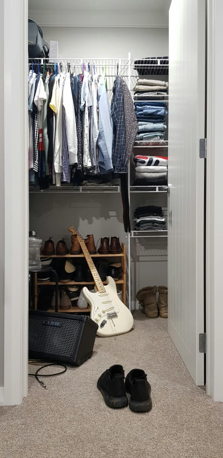 the closet in a bedroom with shoes on the floor and a guitar propped up against the door