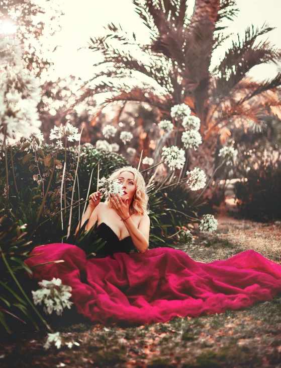 a woman in a pink dress is sitting on the ground near plants