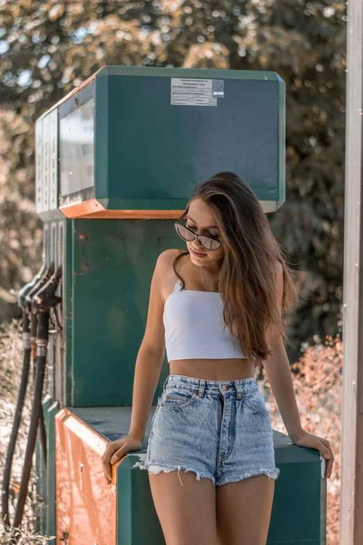 the girl in glasses poses by the gas station's pump