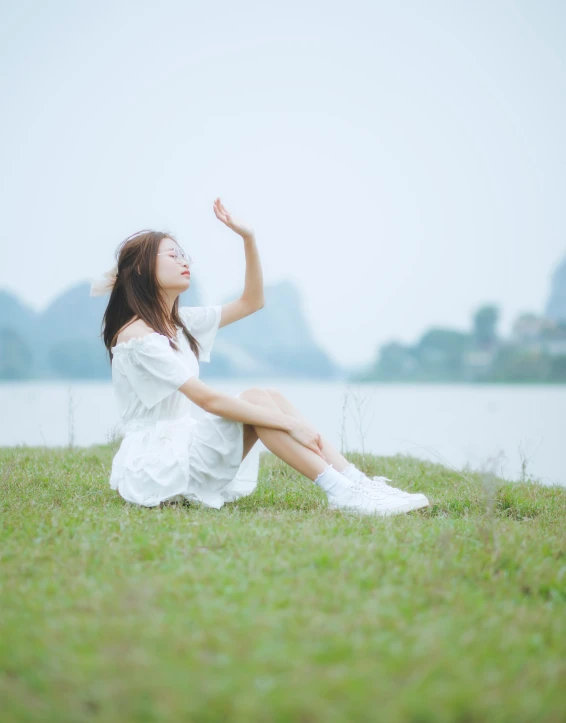 a woman in white is sitting on the grass by the water