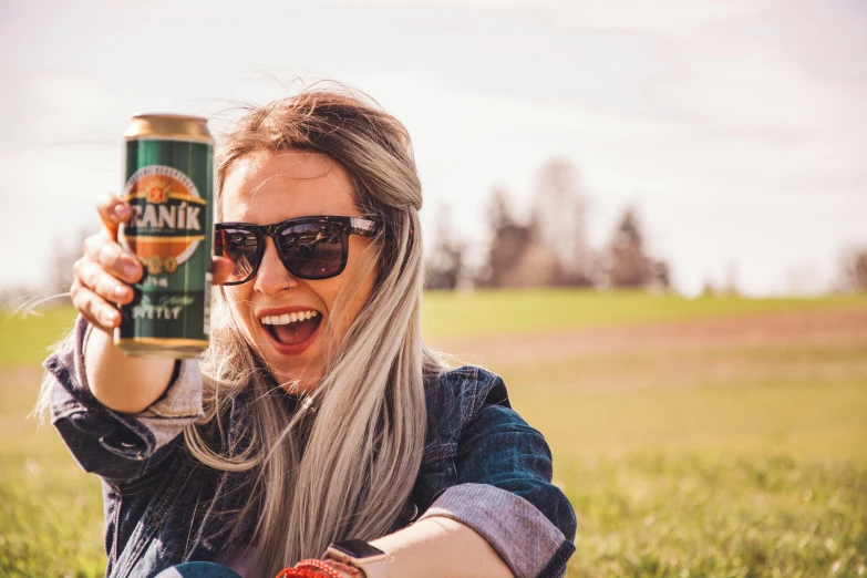 a woman wearing sunglasses holds up a beer