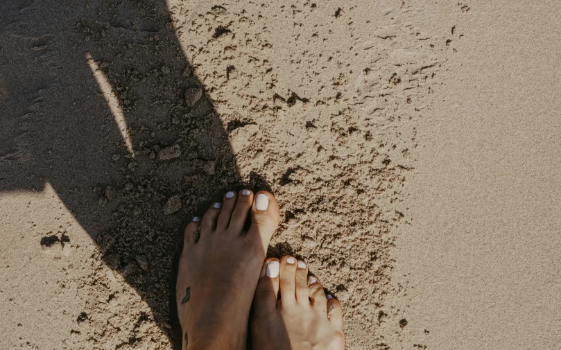 two persons are standing in the sand at the beach